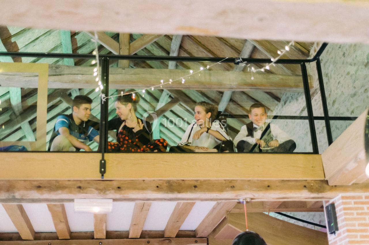 Quatre personnes assises sur une mezzanine en bois, entourées de guirlandes lumineuses, dans un espace au plafond en poutres…