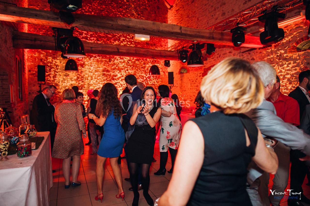 Des personnes dansent et discutent dans une salle en pierre éclairée par des lumières rouges.