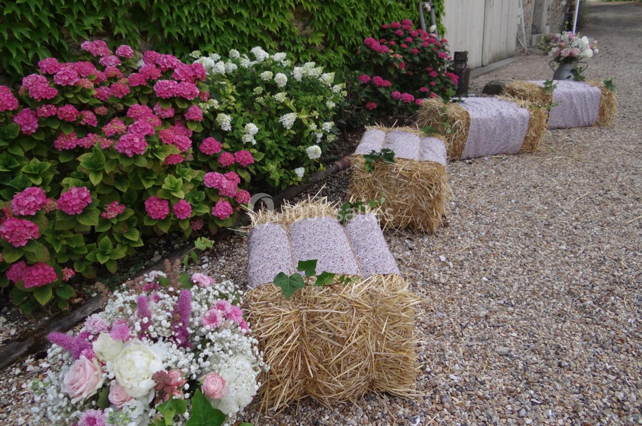 Bottes de paille recouvertes de tissu rose, disposées en rangée, entourées de fleurs et de gravier.
