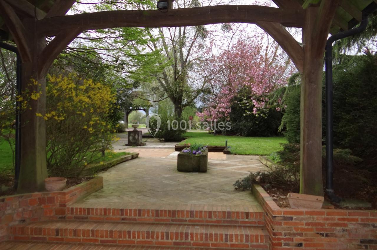 Vue d'un jardin fleuri avec un cerisier en fleurs, encadré par une structure en bois et des marches en briques.