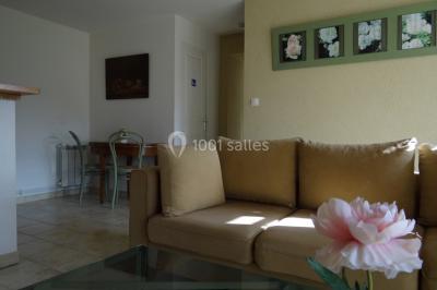 Lit simple avec couvre-lit fleuri dans une chambre lumineuse, éclairée par une lampe de chevet près d'une fenêtre.