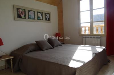 Lit simple avec couvre-lit fleuri dans une chambre lumineuse, éclairée par une lampe de chevet près d'une fenêtre.