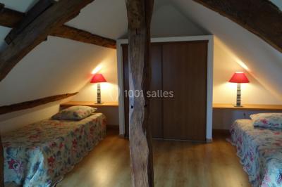 Lit simple avec couvre-lit fleuri dans une chambre lumineuse, éclairée par une lampe de chevet près d'une fenêtre.