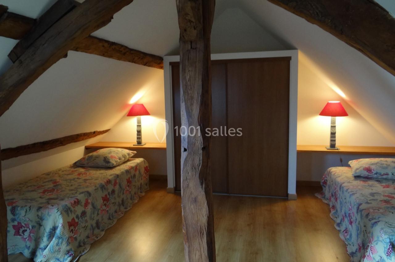 Deux lits simples sous des poutres apparentes dans une chambre mansardée avec lampes de chevet et parquet au sol.