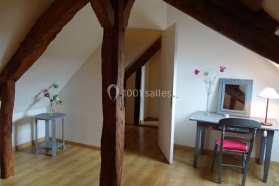 Lit simple avec couvre-lit fleuri dans une chambre lumineuse, éclairée par une lampe de chevet près d'une fenêtre.