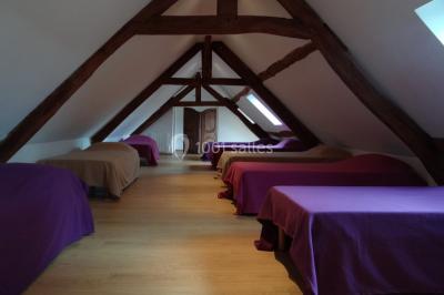 Lit simple avec couvre-lit fleuri dans une chambre lumineuse, éclairée par une lampe de chevet près d'une fenêtre.