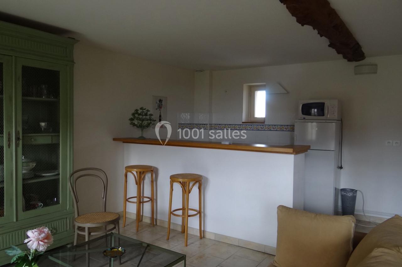 Cuisine ouverte avec un bar en bois, deux tabourets, un réfrigérateur, un micro-ondes et un meuble vert dans un salon…