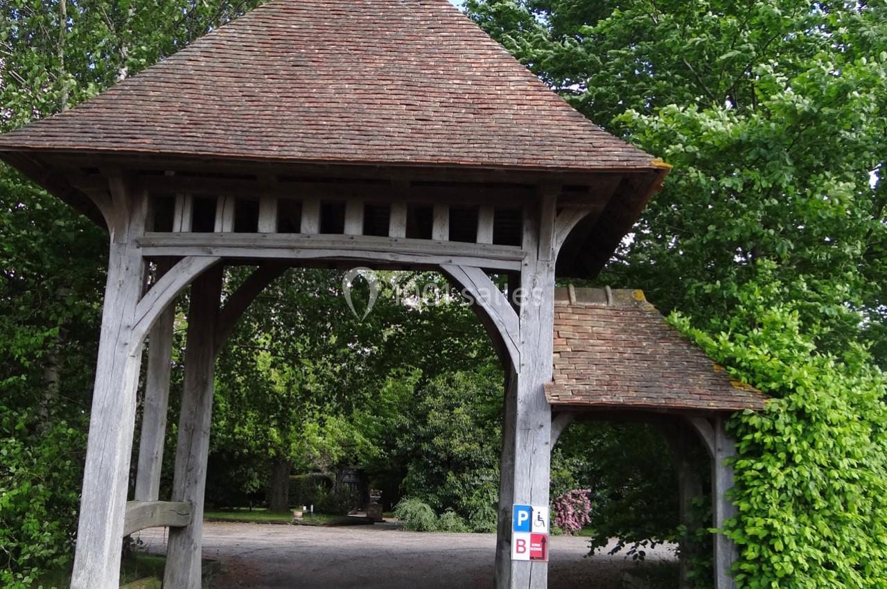 Portail en bois avec toit en tuiles, entouré de végétation, donnant accès à un chemin gravillonné.