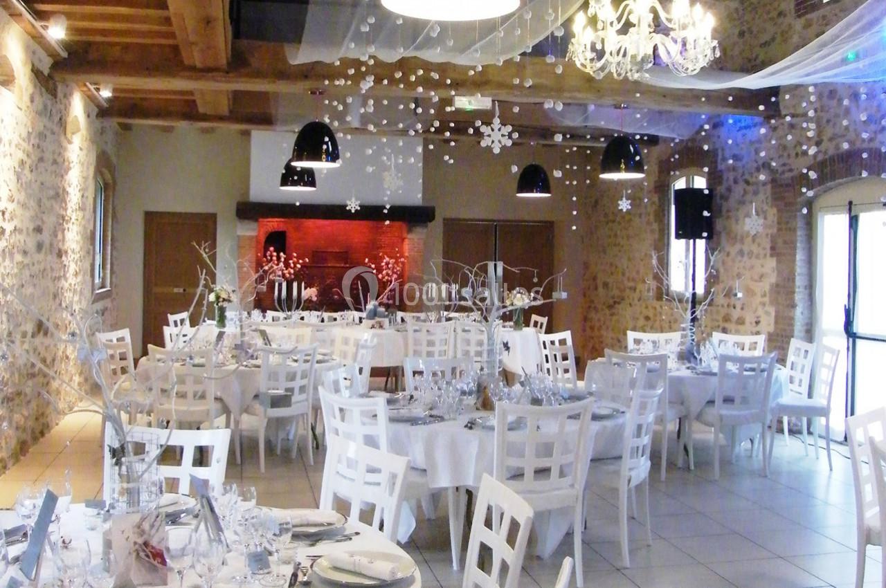 Salle de réception décorée pour un événement, avec tables rondes, chaises blanches et ornements suspendus.