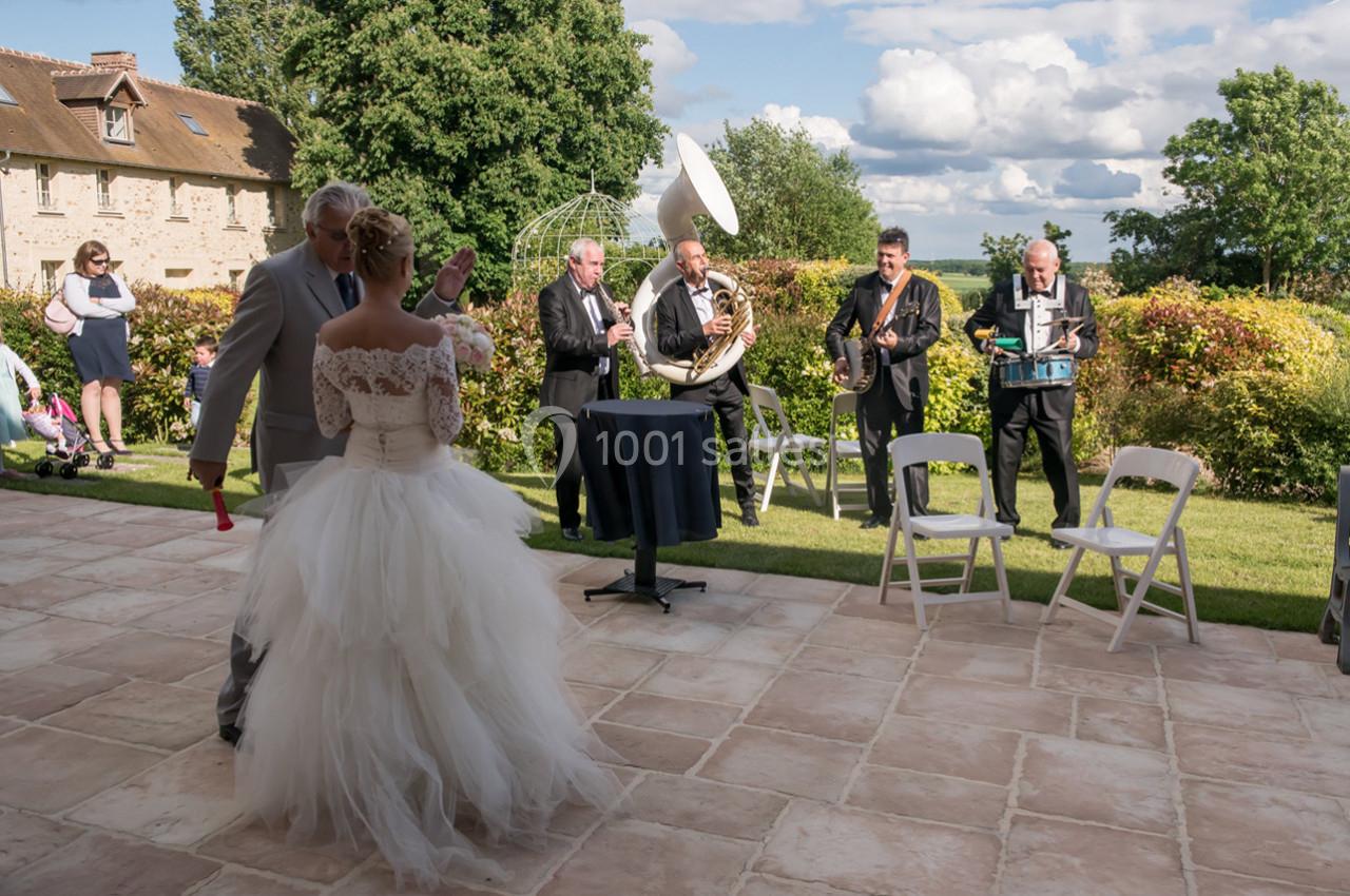Un couple de mariés danse en extérieur devant un groupe de musiciens jouant des instruments à vent et à percussion.