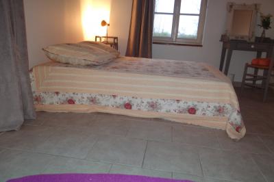 Lit simple avec couvre-lit fleuri dans une chambre lumineuse, éclairée par une lampe de chevet près d'une fenêtre.