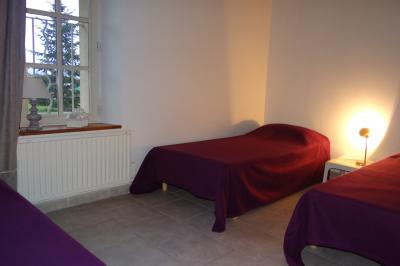 Lit simple avec couvre-lit fleuri dans une chambre lumineuse, éclairée par une lampe de chevet près d'une fenêtre.