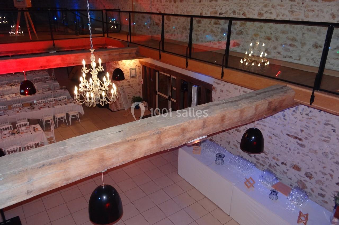 Salle de réception avec tables dressées, lustres suspendus et mezzanine en bois et verre.