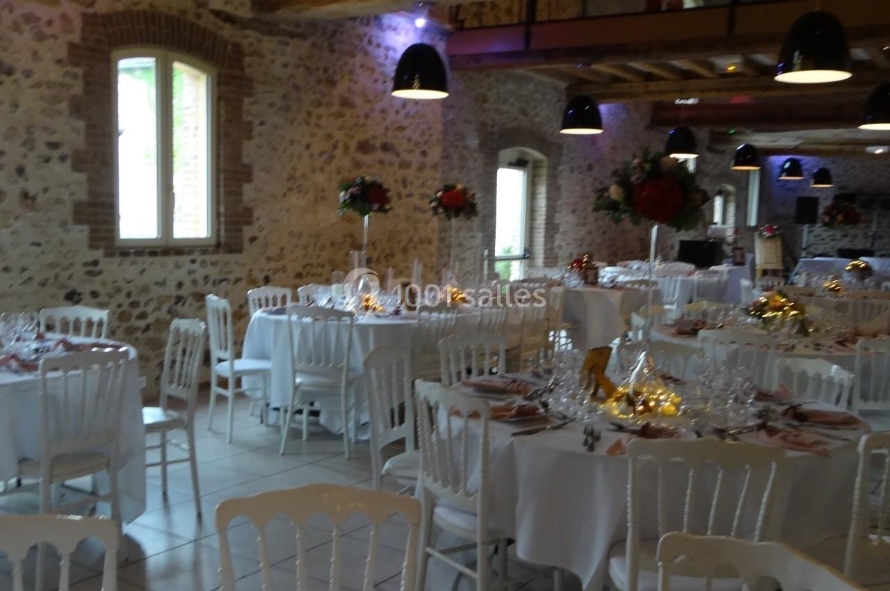 Salle de réception en pierre avec tables rondes dressées, décorations florales et éclairage suspendu.