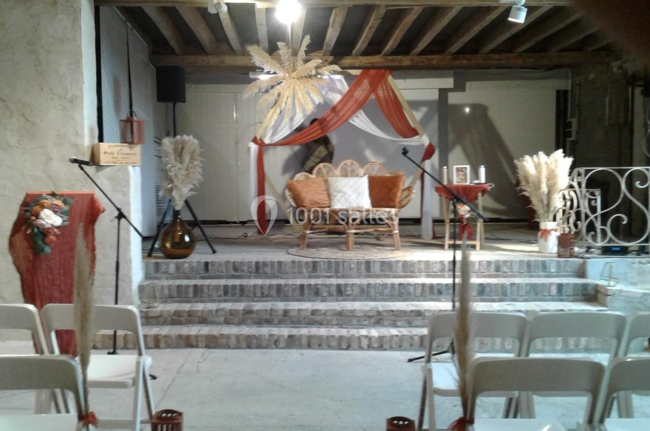 Scène décorée avec des fauteuils en rotin, voilages rouges et blancs, et ornements de pampas, vue depuis des chaises…