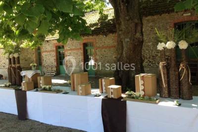 Cour extérieure éclairée en soirée, avec un grand arbre central, des tables, des palettes en bois et des invités debout.