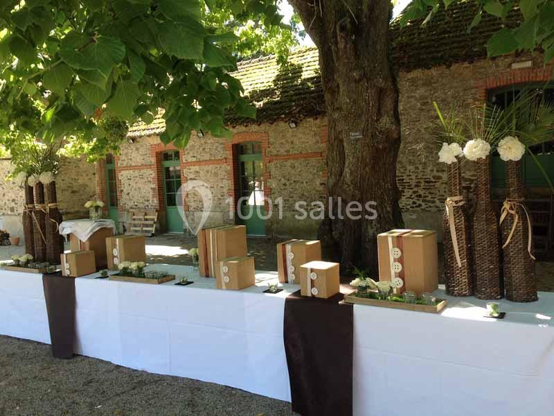 Table décorée en extérieur avec des boîtes en bois, des vases en osier et des fleurs blanches sous un grand arbre.
