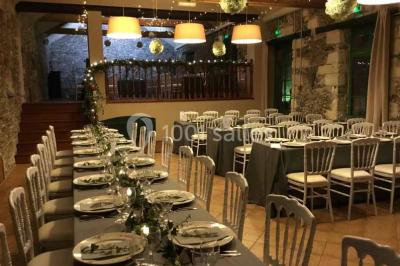 Cour extérieure éclairée en soirée, avec un grand arbre central, des tables, des palettes en bois et des invités debout.