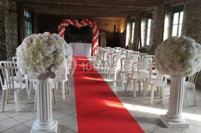 Cour extérieure éclairée en soirée, avec un grand arbre central, des tables, des palettes en bois et des invités debout.