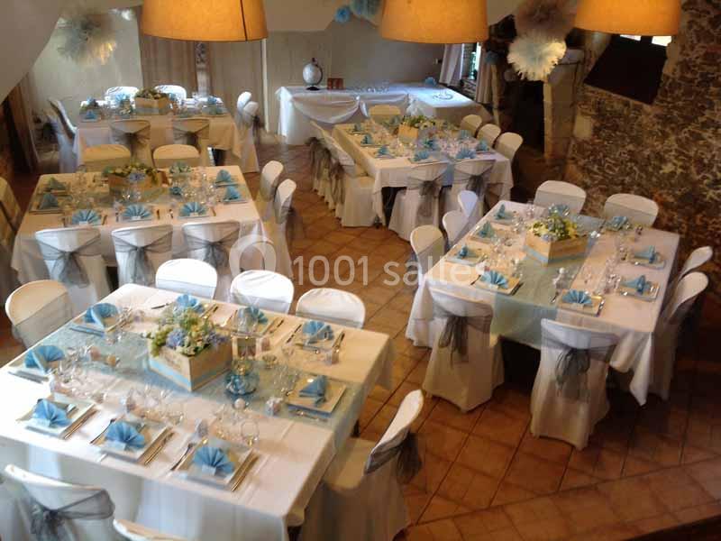 Salle de réception décorée avec des tables dressées, nappes blanches, serviettes bleues et centres de table fleuris.
