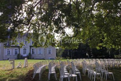 Cour extérieure éclairée en soirée, avec un grand arbre central, des tables, des palettes en bois et des invités debout.