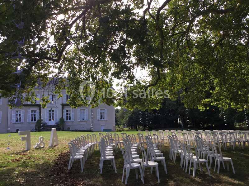 Chaises blanches disposées en rangées sur une pelouse ombragée devant un bâtiment ancien, préparées pour un événement.