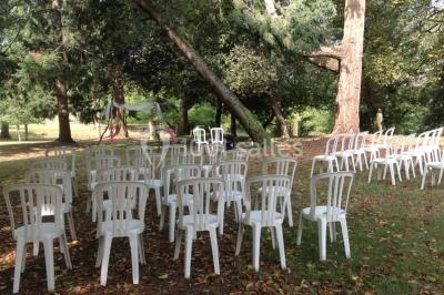 Cour extérieure éclairée en soirée, avec un grand arbre central, des tables, des palettes en bois et des invités debout.