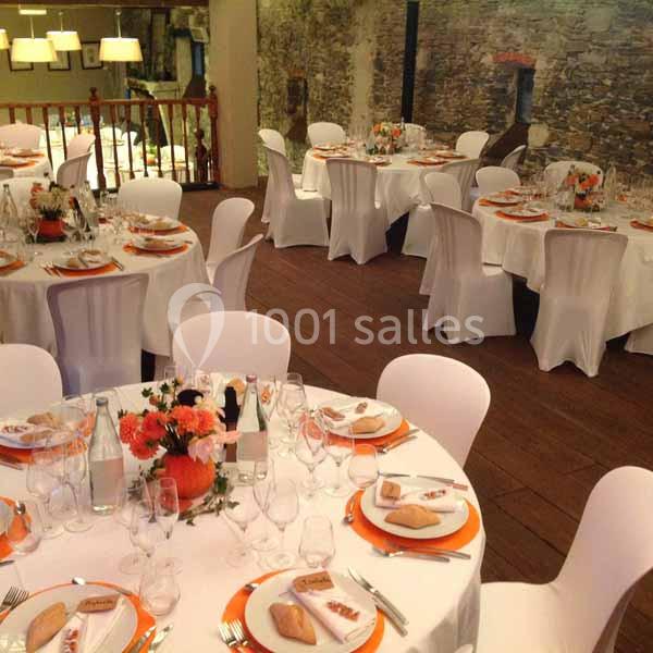 Salle de réception avec tables rondes dressées, nappes blanches, décorations orange et centres de table fleuris.