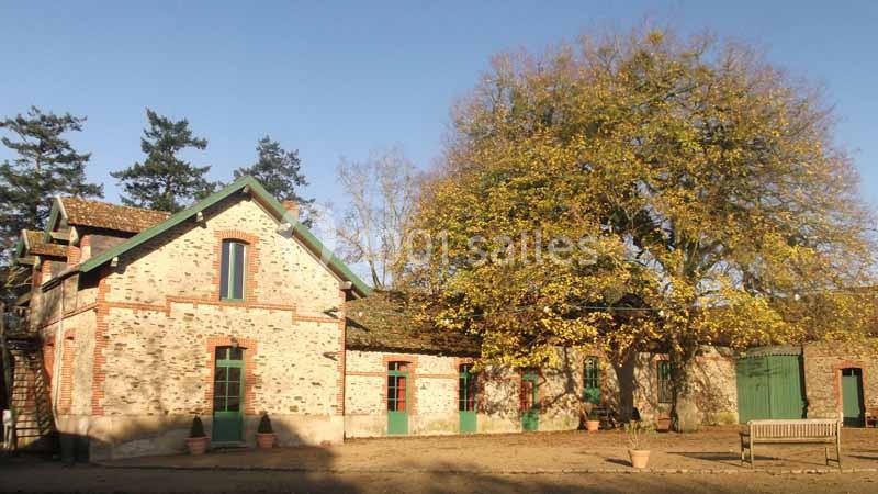 Bâtiment en briques rouges avec des volets verts, entouré d'arbres et baigné par une lumière ensoleillée.