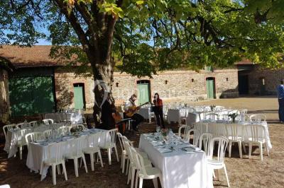Cour extérieure éclairée en soirée, avec un grand arbre central, des tables, des palettes en bois et des invités debout.