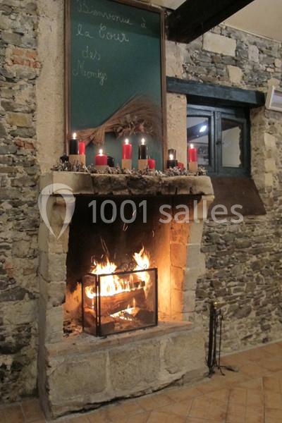 Cheminée en pierre allumée, décorée de bougies rouges sur le manteau, dans une pièce aux murs en pierre apparente.
