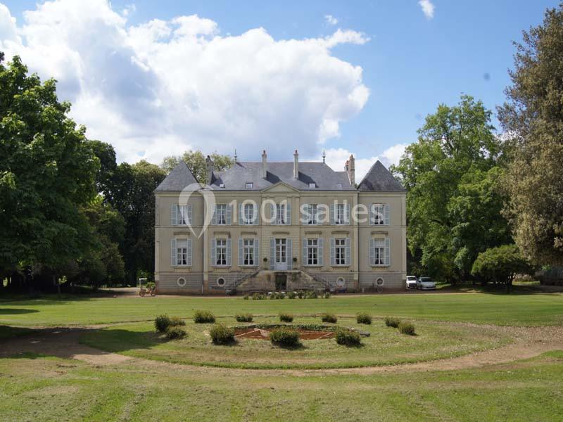 Façade d'un château en pierre entouré de pelouses et d'arbres sous un ciel partiellement nuageux.