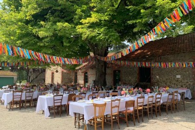 Un groupe de personnes rassemblées sous de grands arbres devant des bâtiments en pierre par une journée ensoleillée.