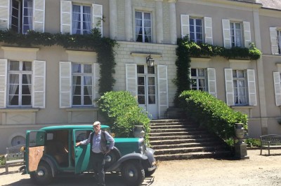 Un groupe de personnes rassemblées sous de grands arbres devant des bâtiments en pierre par une journée ensoleillée.