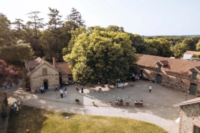 Un groupe de personnes rassemblées sous de grands arbres devant des bâtiments en pierre par une journée ensoleillée.