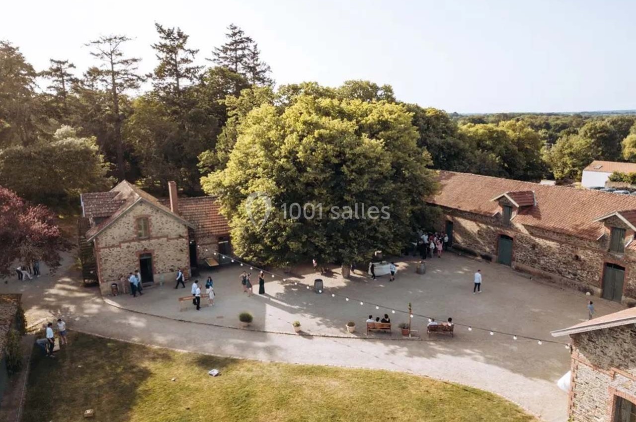 Vue aérienne d'une cour entourée de bâtiments en pierre, avec des arbres et des personnes rassemblées en petits groupes.