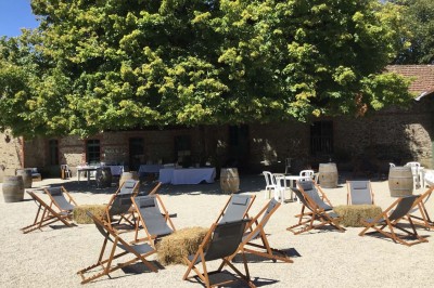 Un groupe de personnes rassemblées sous de grands arbres devant des bâtiments en pierre par une journée ensoleillée.