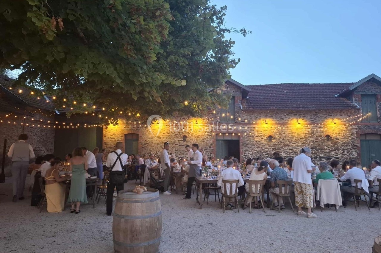 Repas en plein air sous des guirlandes lumineuses devant un bâtiment en pierre, avec des convives attablés.