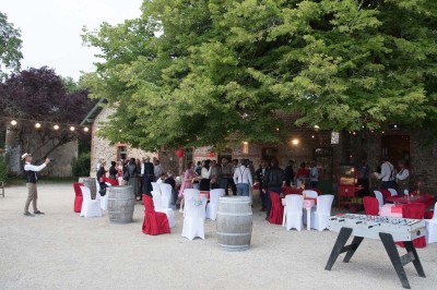 Un groupe de personnes rassemblées sous de grands arbres devant des bâtiments en pierre par une journée ensoleillée.