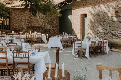 Un groupe de personnes rassemblées sous de grands arbres devant des bâtiments en pierre par une journée ensoleillée.