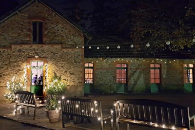 Un groupe de personnes rassemblées sous de grands arbres devant des bâtiments en pierre par une journée ensoleillée.