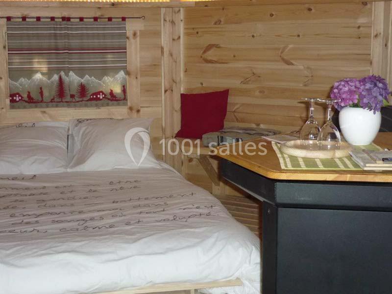 Chambre en bois avec lit double, décoration alpine, table avec vase de fleurs violettes et verres à pied.