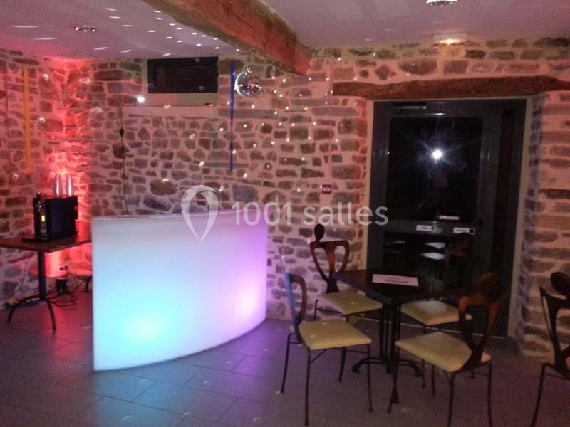 Salle avec murs en pierre, comptoir lumineux, chaises et tables, éclairage tamisé et ambiance festive.