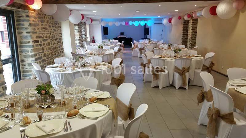 Salle de réception décorée avec des tables rondes dressées, nappes blanches et chaises ornées de nœuds en toile de jute.