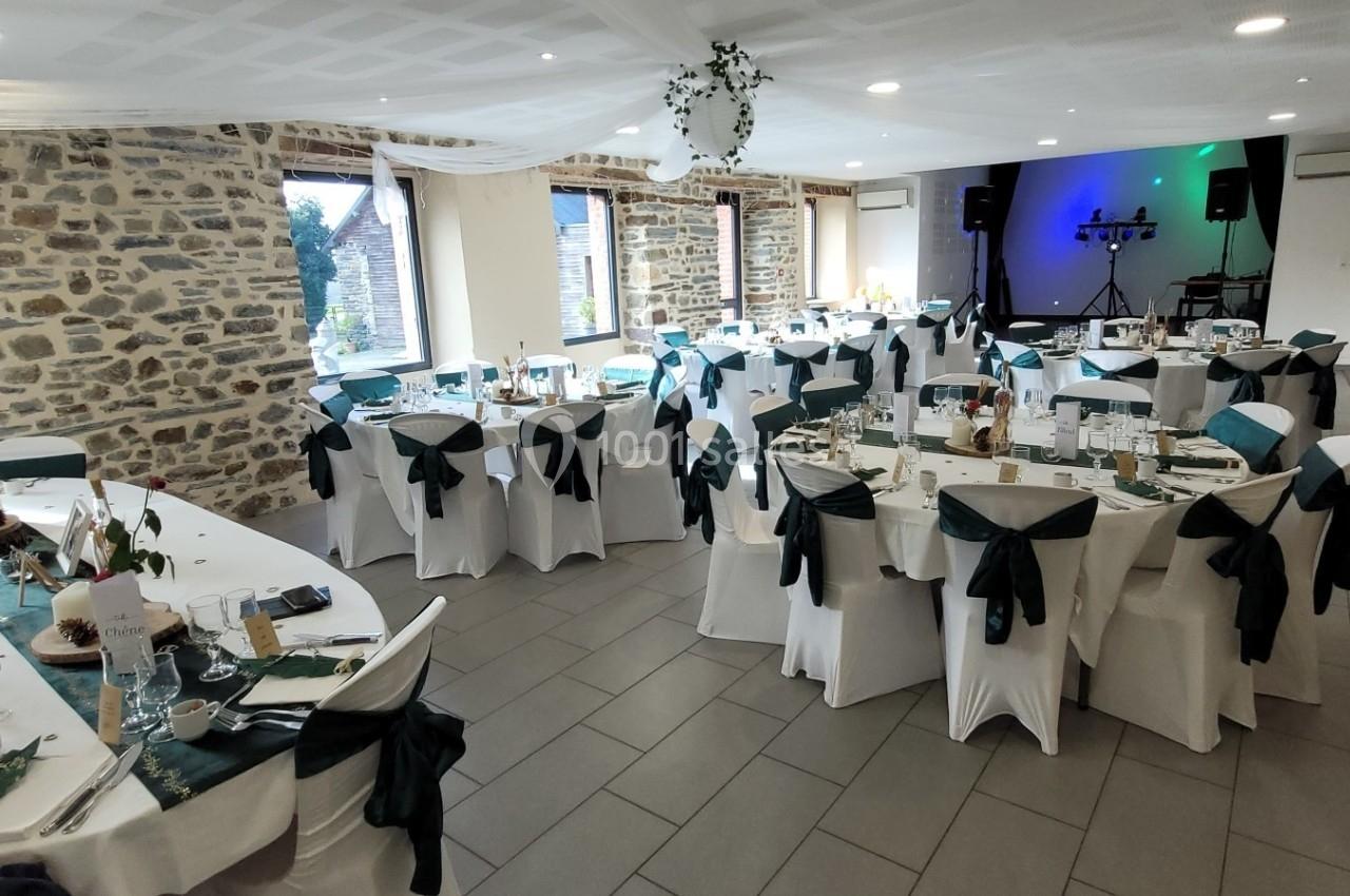 Salle de réception décorée avec des tables rondes dressées, nappes blanches et chaises ornées de nœuds verts.