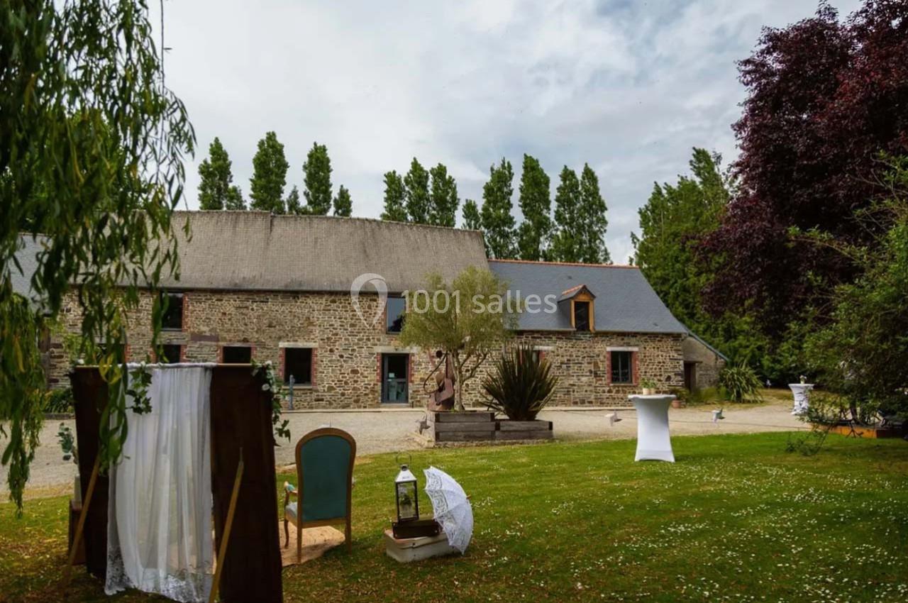 Bâtiment en pierre avec toit en ardoise, entouré d'arbres, pelouse aménagée avec mobilier et décorations.