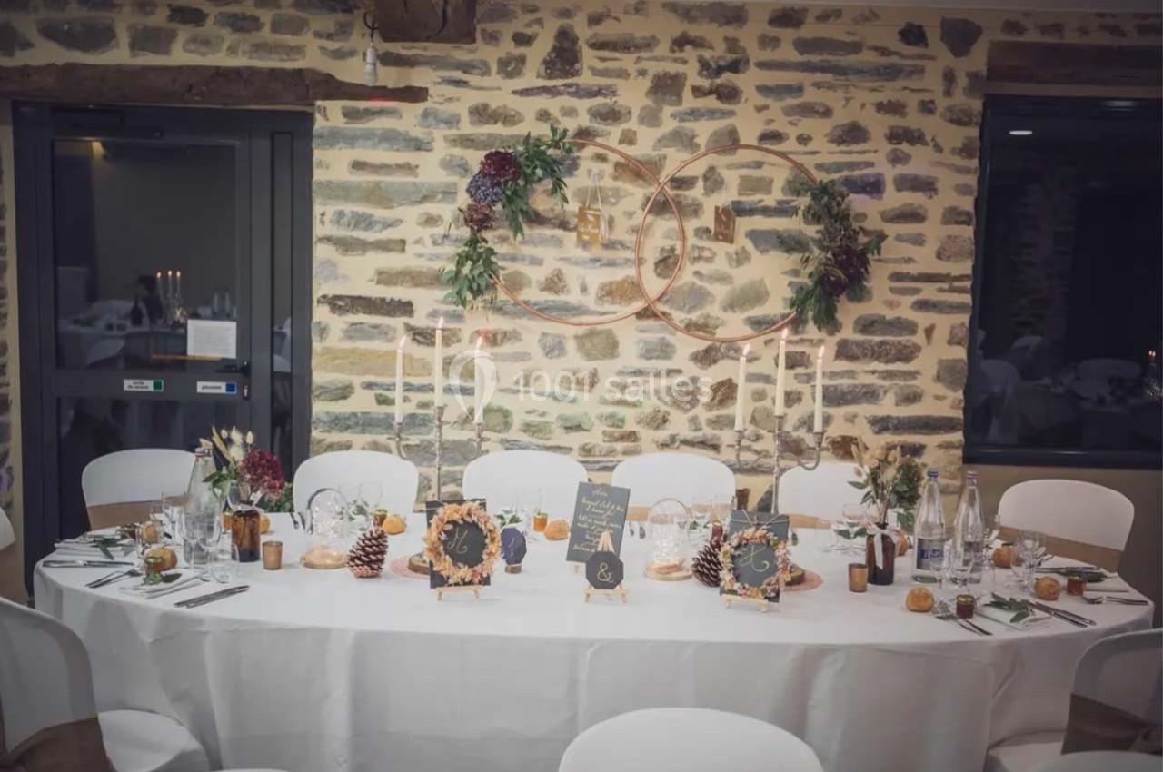 Table décorée pour un dîner, avec bougies, fleurs, éléments rustiques et un mur en pierre en arrière-plan.