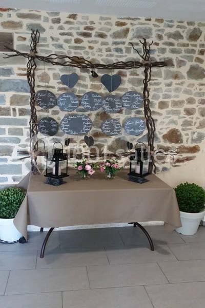Table décorée avec une nappe beige, lanternes noires, bouquets de fleurs et fond en pierre avec ardoises suspendues.