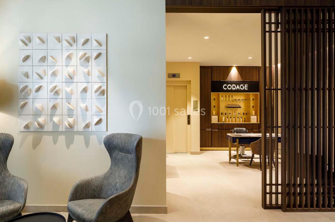 Deux fauteuils gris et une table basse dans un espace lumineux, avec un mur décoratif et un accès à une pièce adjacente.