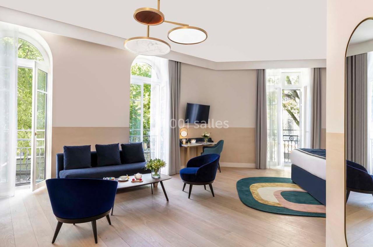 Salon lumineux avec canapé bleu, fauteuils assortis, table basse, tapis coloré et grandes fenêtres donnant sur la verdure.